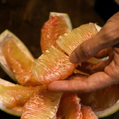 Pomelo fruit skin with pink membrane on dark wood table and hand peel it
