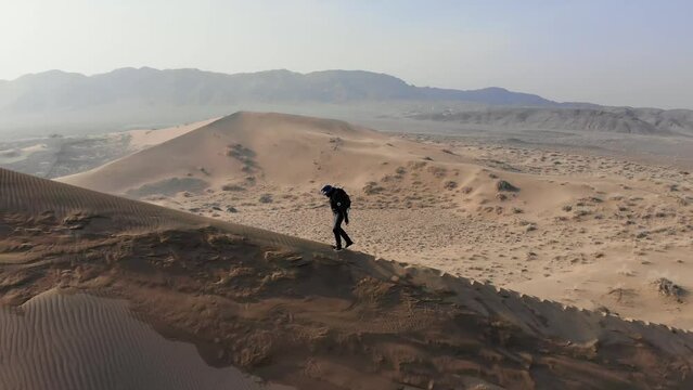 A traveller climbing up a sand dune. View from the side. Cold season in the desert. Shooting from a drone