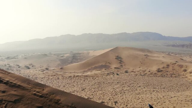 A male tourist standing on the ridge of a barkhan against the background of a mountainous desert landscape. Singing Barkhan. Altyn-Emel National Park