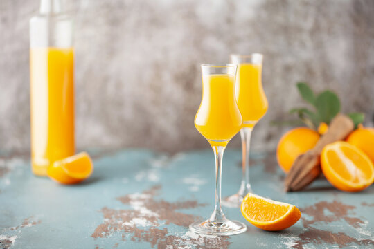 Arancello in grappas wineglass, sweet Italian orange liqueur, traditional strong alcoholic drink and oranges on the light blue wooden background.