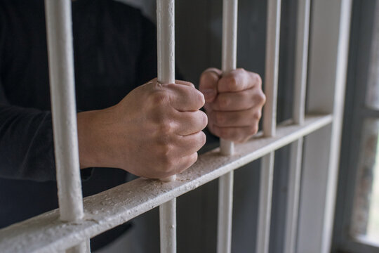 檻に閉じ込められた男性の手　鉄格子を掴む刑務所の犯罪者　Hands of prisoner holding bars in jail