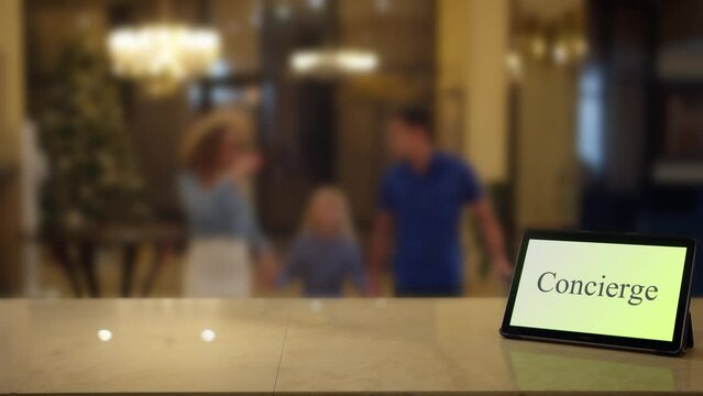 A family on holiday in a hotel approaches to the reception desk with a tablet labeled concierge