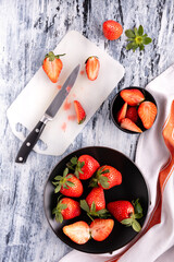 top view, a bowl and a black plate with delicious whole and sliced red strawberries on the cutting board