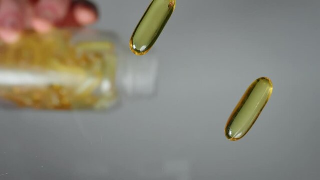 Vitamine E, fish oil capsules spill out of a transparent plastic container jar on a transparent table