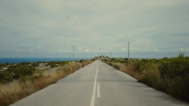 Camera slowly moves over quiet empty country road to lighthouse standing in distance. Travel and exploring concept in far away destination. Calm and peace, copy space cinematic background