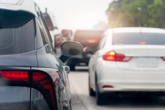 Rear side of a grey car on the road with other cars driving on the road. Blurred background of trees under white sky.