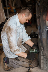 Fototapeta na wymiar A mechanic repairs a car chassis. A man removes car wheels using a pneumatic screwdriver