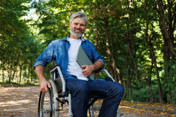 Fototapeta premium Adaptive Workspaces: Wheelchair User Utilizing Laptop in Natural Setting