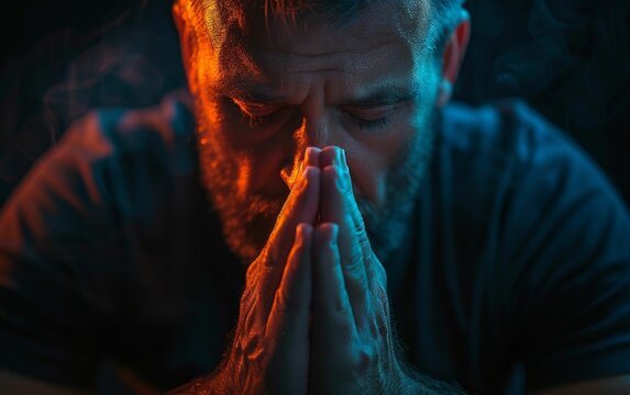 A multiracial man stands with his hands clasped in prayer