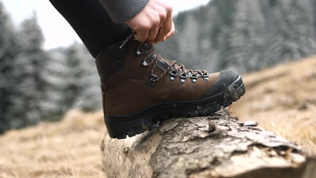 Close up of woman hiker wearing brown mountain boots tying shoelaces on a log in early spring season.