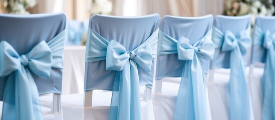 A row of chairs covered in blue fabric and adorned with bows, set up in a wedding hall or event space. The chairs are neatly arranged in a line, adding a touch of elegance to the decor.