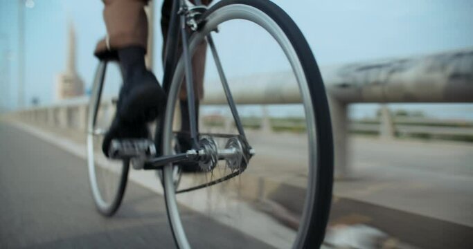 Close up shot of commuter cyclist pedal hard on single speed city bike. Man ride a bicycle on bike lane in urban city district. Spinning wheel, freehub and chainring