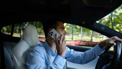 Profile of confident businessman driving electric car on urban road and talking on phone. Male businessperson operating electrical vehicle at city and speaking by smartphone. Concept of business - 754395496