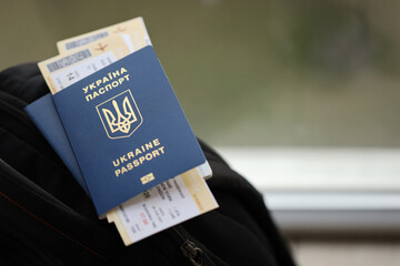 Two ukrainian biometrical passports with air flight tickets on black touristic backpack close up - obrazy, fototapety, plakaty