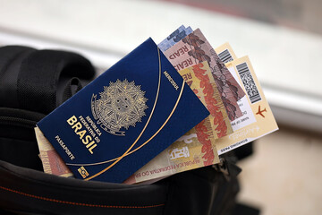 Blue Brazilian passport with money and airline tickets on touristic backpack close up. Tourism and...