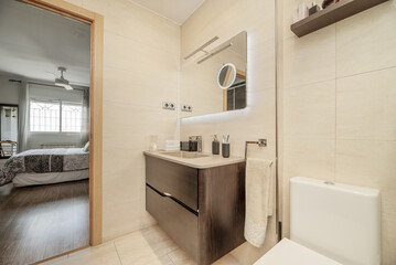 Fototapeta na wymiar Small bathroom with porcelain toilets, dark cabinet with drawers, mirror with USB lights and shower cabin with tempered glass screens