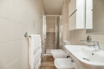 Small bathroom with white porcelain toilets, mirror with lights and shower cabin with glass screens