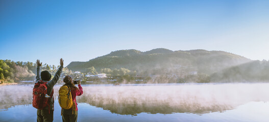 An Asian couple who is standing and watching the fog rising on the lake in the morning. Travel Ban Rak Thai village, Mae Hong Son in Thailand. Take a picture of the lake - 754410891