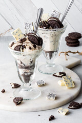 Two chocolate sandwich cookie ice cream parfaits with ingredients all around.