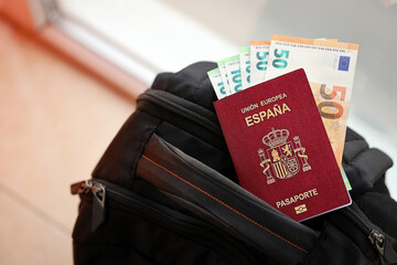Red Spanish passport of European Union with money and airline tickets on touristic backpack close...