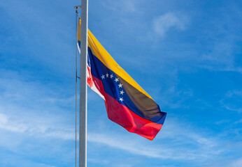 Venezuelan flag on a flagpole against a blue sky Venezuelan flag flutters in the wind against a sky with clouds