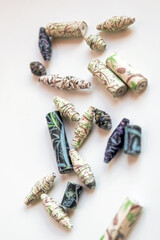 Handmade paper beads of brown, green, black colored floral patterns lying on white table