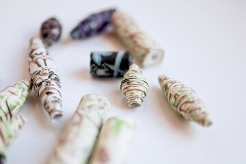 Handmade paper beads of brown, green, black colored floral patterns lying on white table side view