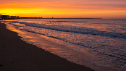 Amazing view of a fiery sunrise with multicolored clouds. Sea waves along the seashore at sunrise. Morning time. Ocean view. La Baule-Escoublac, France