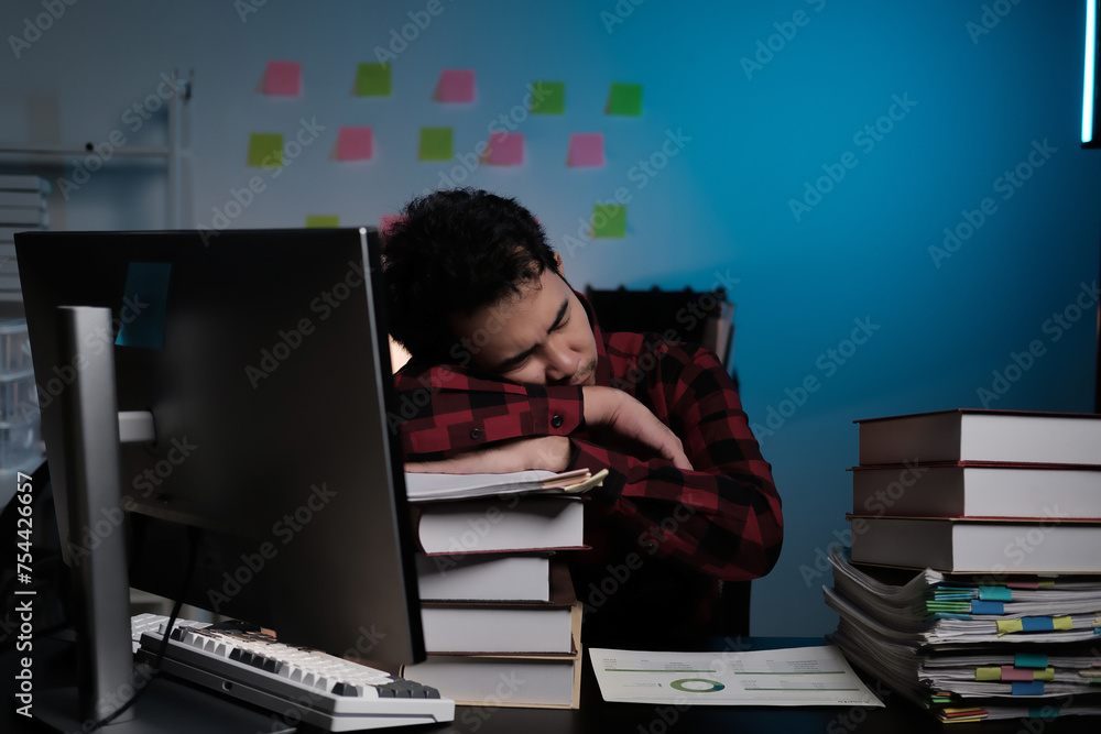 Poster A man is sleeping on his desk with a computer monitor and stacks of books