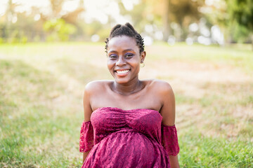 Happy African pregnant woman smiling on camera in a public park - Maternity lifestyle concept