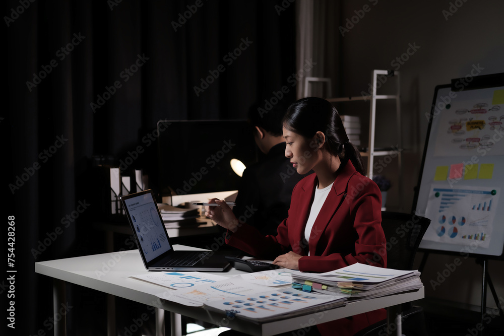 Poster a woman in a red jacket is sitting at a desk with a laptop and a stack of papers
