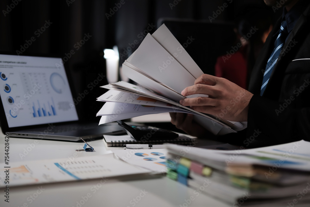 Poster a man is holding a stack of papers and looking at a laptop