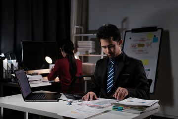 A man in a suit is sitting at a desk with a laptop and papers