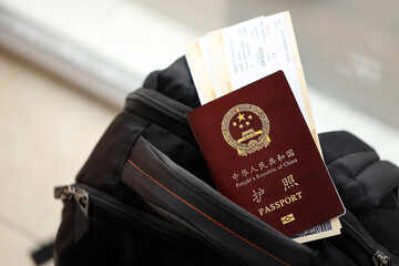Red passport of People Republic of China with airline tickets on backpack close up. PRC passport
