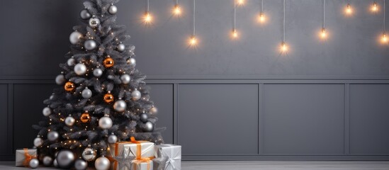 A Christmas tree adorned with shimmering silver and vibrant orange ornaments stands in a cozy interior with a gray wall background. The tree is illuminated with twinkling garlands and shiny baubles,