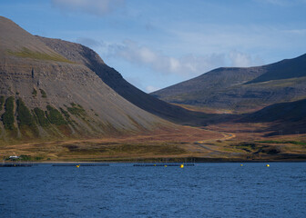 Aquaculture in Westfjords, Iceland - fish farming in circular nets on open sea in fjord and mountain pass road in background