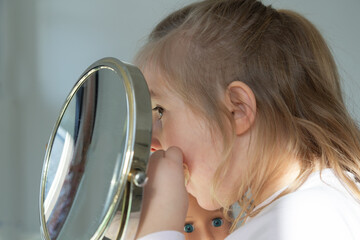 Five-year old little girl standing holding her doll while looking into a round mirror