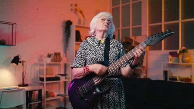 Humorous grandmother playing an electric guitar and singing song at home, hobby