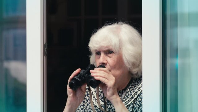 Comic senior woman spying on her neighbors through the window using binoculars