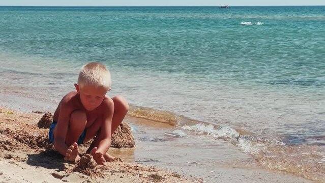 A boy plays a sand constructor, spending healthy leisure time on the Black Sea beach. A child builds a sand castle. A boy who builds a sand fortress on the seashore on a sunny day. 4K