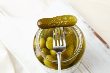 Pickled cucumbers on a fork and in a jar on a wooden background. Homemade pickles. Top view.