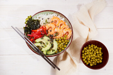 Poke bowl with shrimp, rice, avocado, pepper, green peas, nori and micro greens on a white wooden background. 