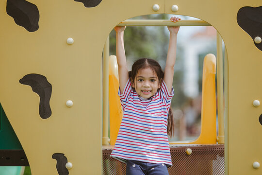 Happy little girl having fun on the playground in summertime with her hands up