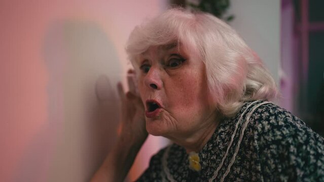 Humorous granny eavesdropping on her neighbors through the wall, funny woman
