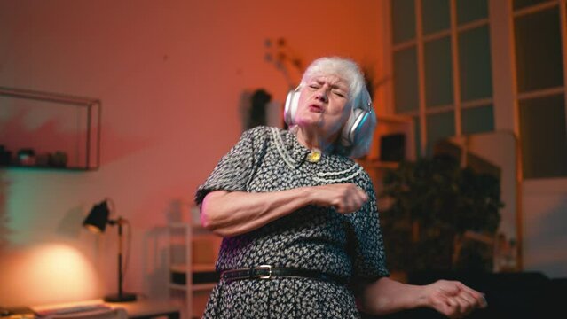 Funny grandma in headphones dancing to the music and having fun at home, joy