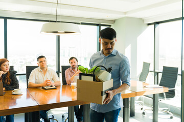 Sad looking Hispanic man getting his stuff in a box and leaving the office after getting fired