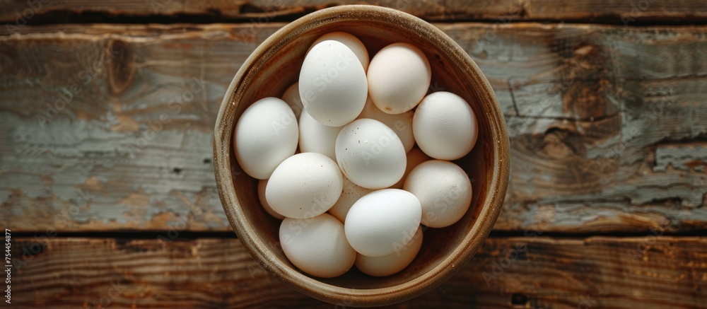 Poster white eggs are neatly arranged in a bowl placed on a rough wooden table, creating a simple yet elega