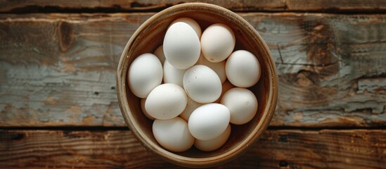 White eggs are neatly arranged in a bowl placed on a rough wooden table, creating a simple yet elegant display.