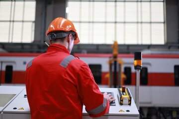 The male railway engineer wearing a red safety suit is working on the control unit in the maintenance garage.
