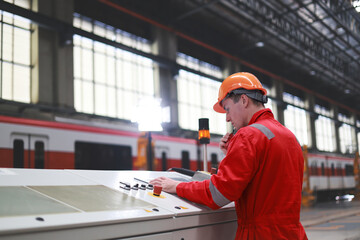 The male railway engineer wearing a red safety suit is working on the control unit in the...